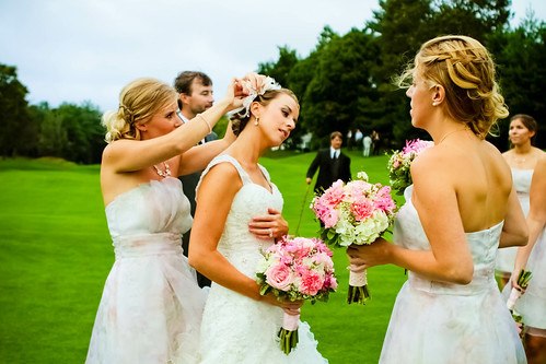 Bridesmaids help the bride prepare for her wedding at an outdoor venue.