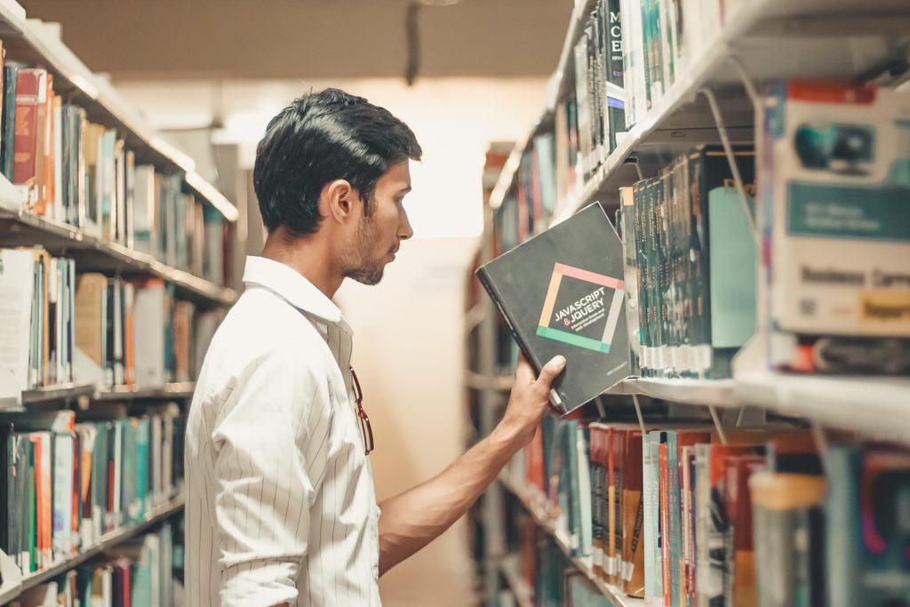 A man pulling a book on javascript and jquery from the shelf of his local public library.